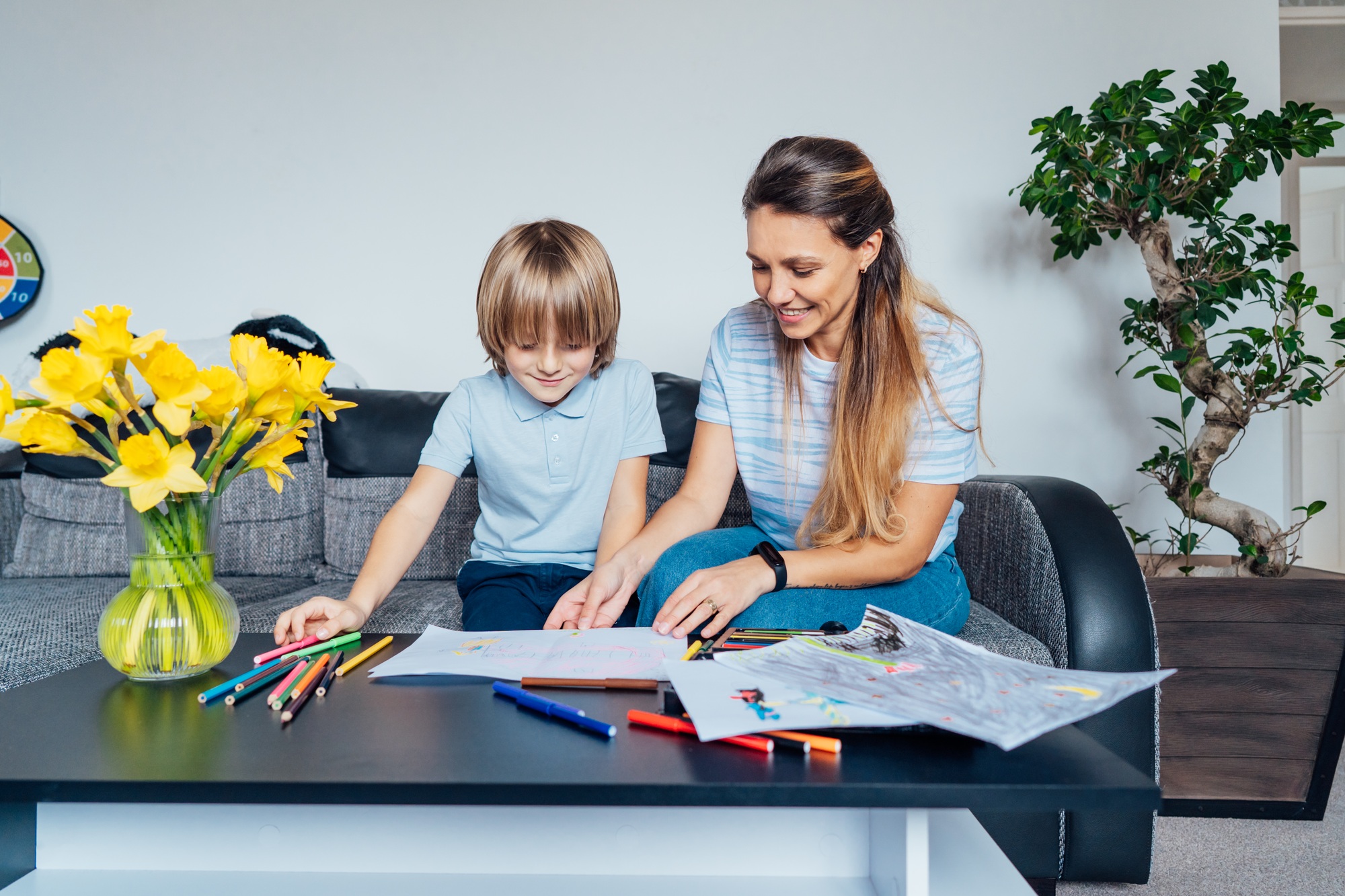 Mother and son drawing with color pencils and markers in the living room. Child creativity concept.